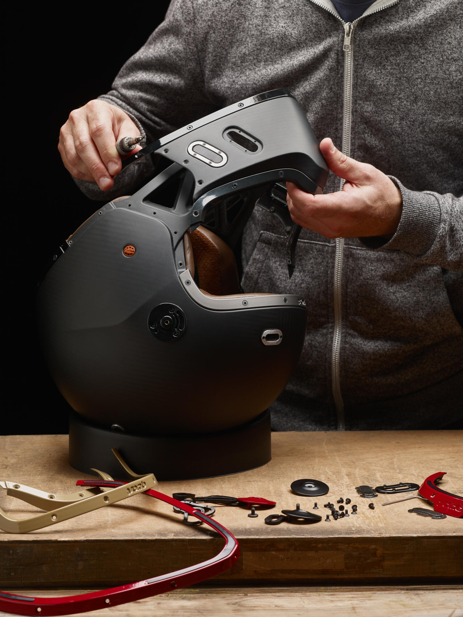 Photographie professionnelle de l'assemblage d'un casque de moto noir modulaire, avec mains et pièces détachées sur une table. Image réalisée par Studio ZE, photographe d'objet technique à Toulouse.