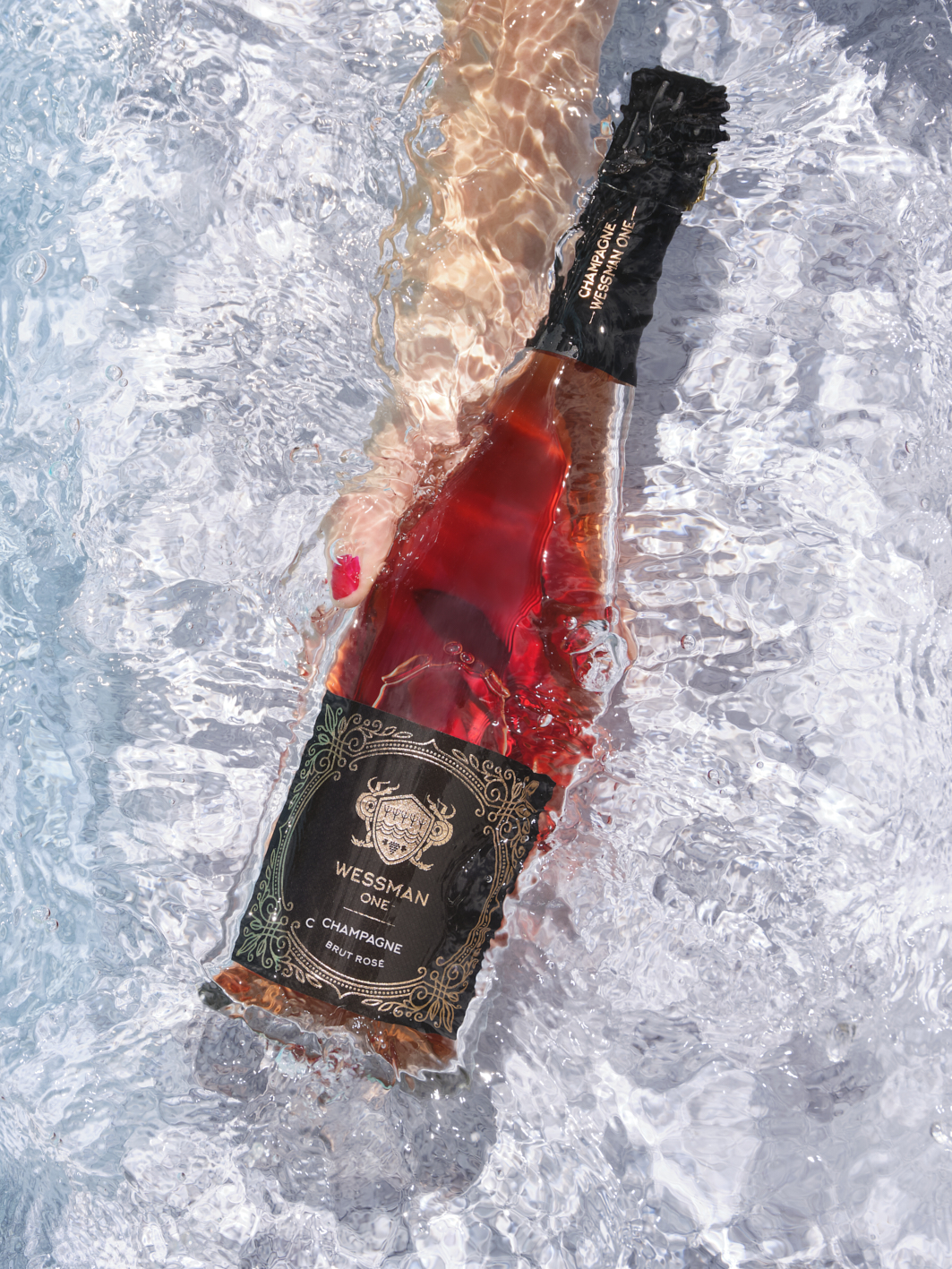 Photographie professionnelle d'une bouteille de Champagne Rosé Wessman One partiellement immergée dans l'eau, avec des bulles et la main d'une personne. Image réalisée par Studio ZE, photographe culinaire de boissons à Toulouse.