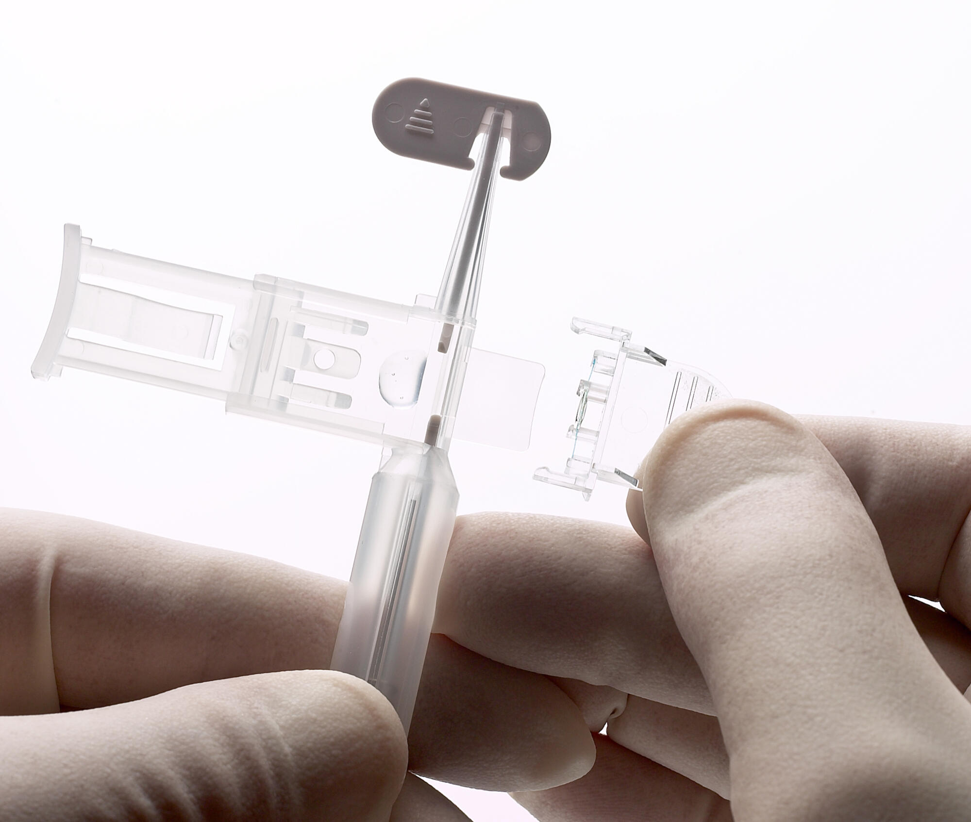 Photographie professionnelle en gros plan de mains gantées assemblant un petit dispositif médical en plastique transparent. Image réalisée par Studio ZE, photographe d'objet technique et médical à Toulouse.