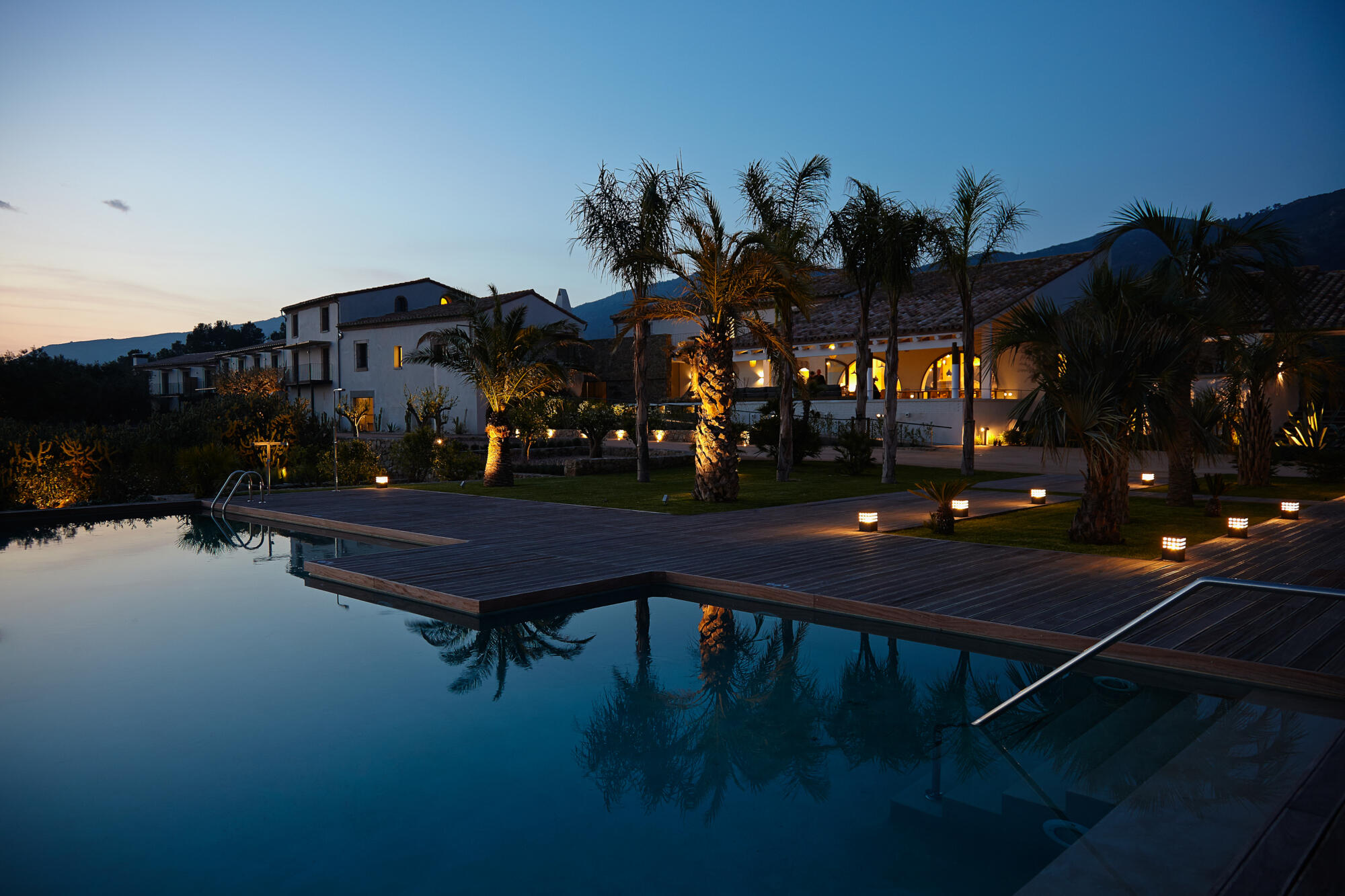 Photographie d'une luxueuse résidence privée avec piscine et palmiers au crépuscule. Par Studio ZE, photographe d'architecture et villas à Toulouse.