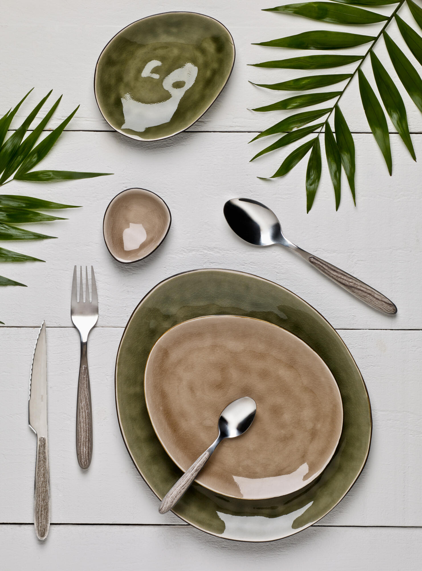 Photographie de vaisselle en céramique aux tons terreux, couverts design et feuilles de palmier. Par Studio ZE, photographe d'art de la table à Toulouse.