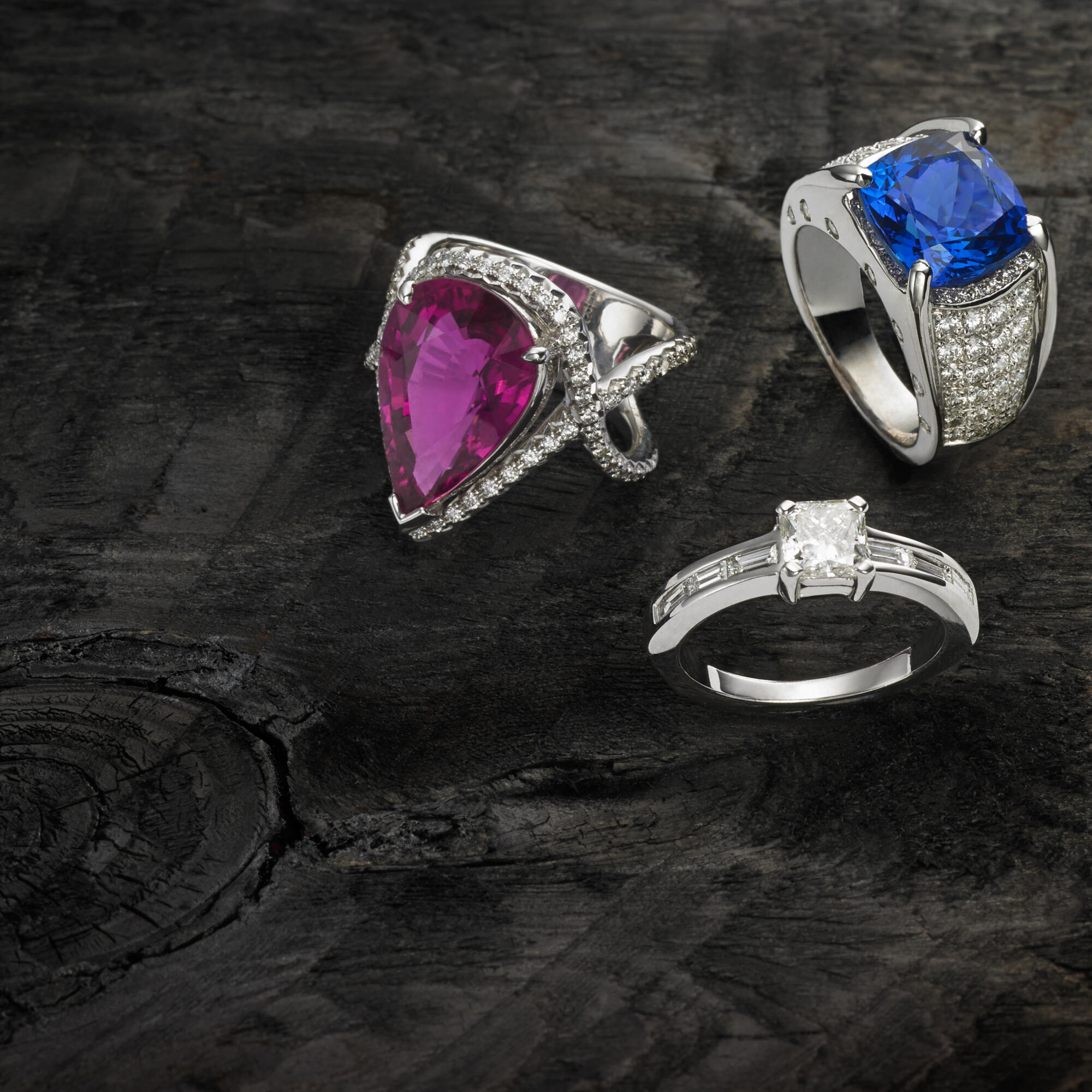 Photographie de bagues de joaillerie avec rubis rose, saphir bleu et diamants sur fond bois sombre. Par Studio ZE, photographe bijoux à Toulouse.