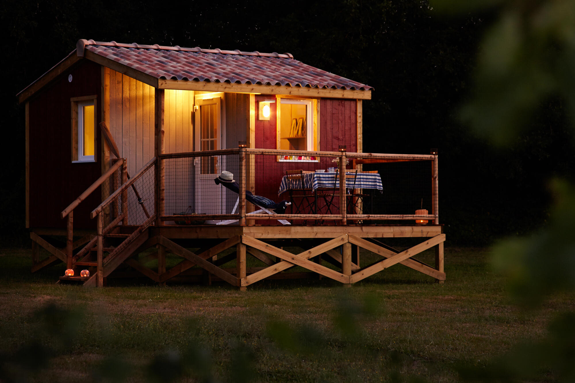 Photographie de nuit d'une petite cabane en bois illuminée avec terrasse, pour hébergement insolite. Par Studio ZE, photographe d'architecture et de gîtes à Toulouse.