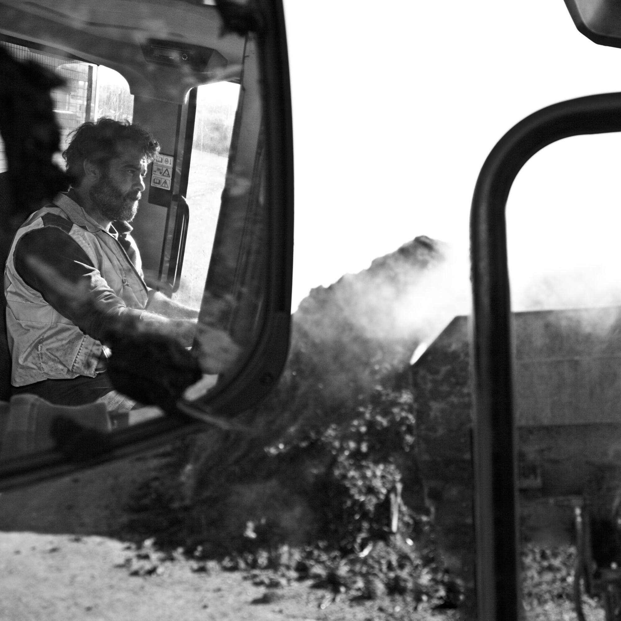 Photographie en noir et blanc d'un homme conduisant un engin de chantier, avec de la terre ou des matériaux à l'extérieur. Par Studio ZE, photographe humain à Toulouse.