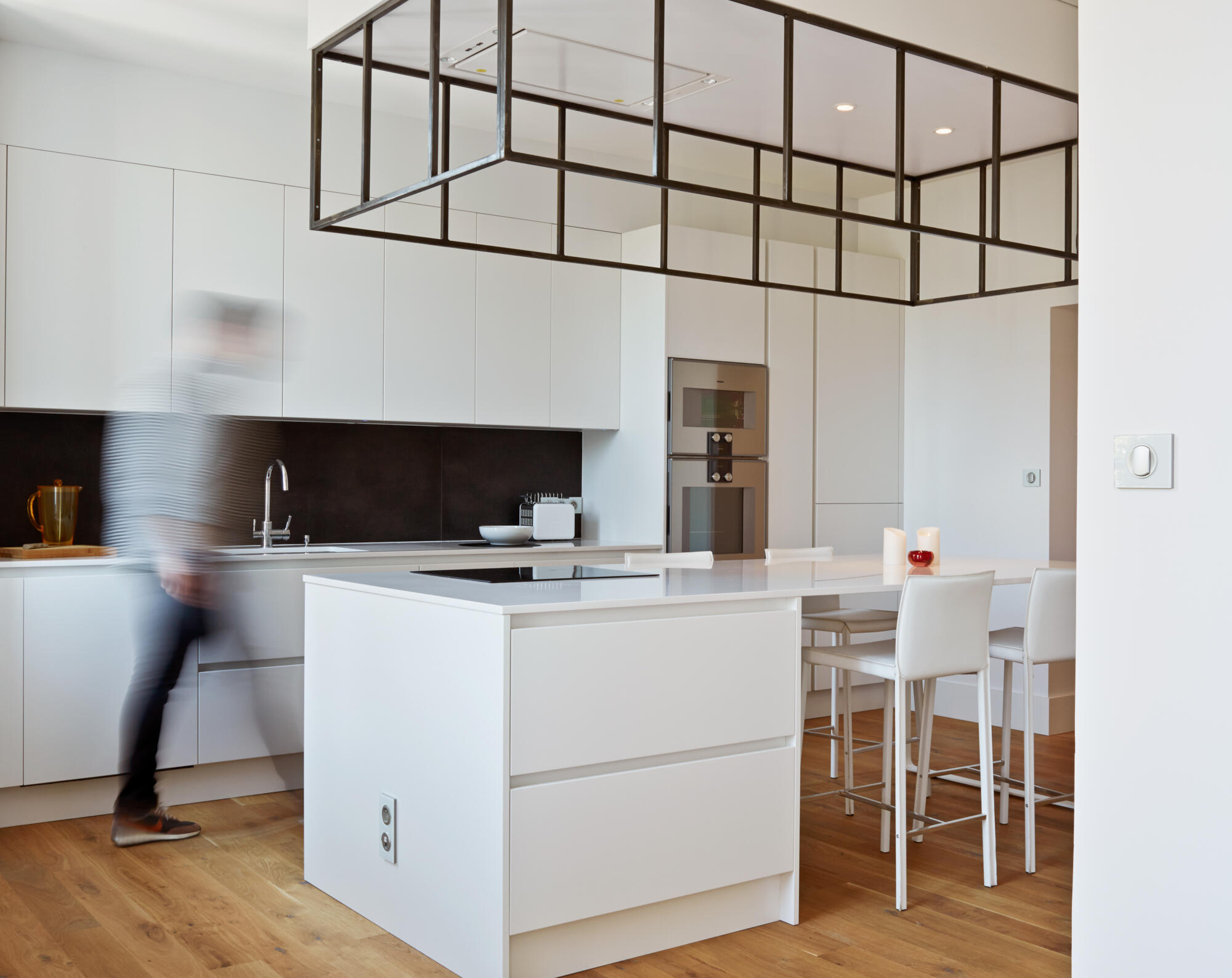 Photographie d'une cuisine moderne blanche avec îlot central, hotte design et parquet clair. Par Studio ZE, photographe d'intérieur à Toulouse.