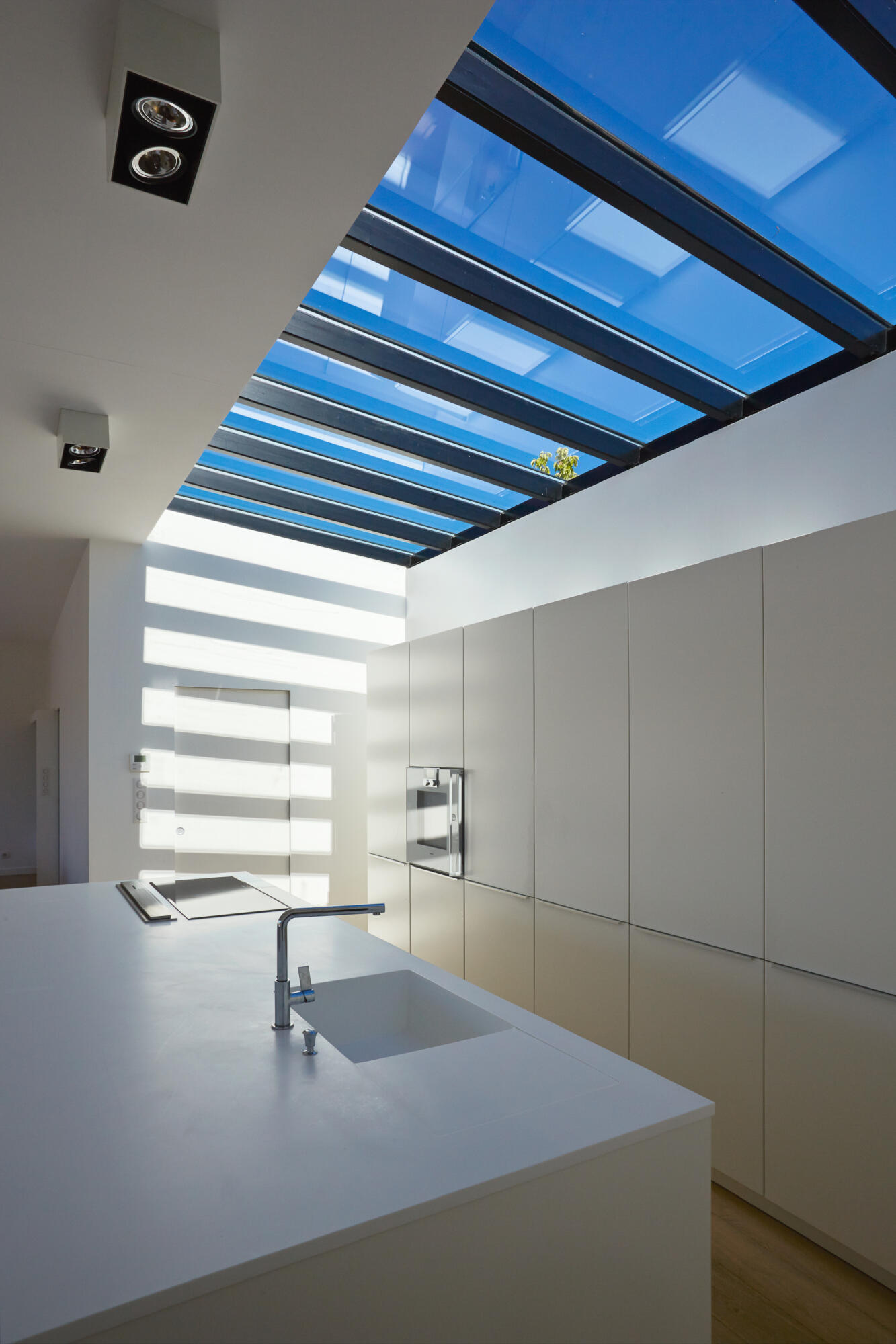 Photographie d'une cuisine moderne et lumineuse avec îlot central, meubles intégrés et grande verrière au plafond. Par Studio ZE, photographe d'intérieur à Toulouse.
