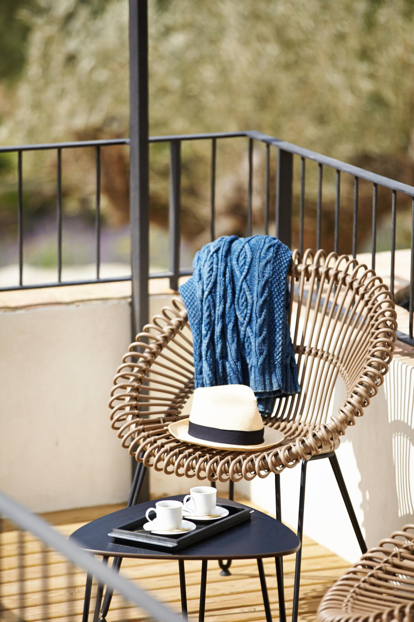 Photographie de mobilier d'extérieur avec fauteuil en rotin, table basse et tasses à café sur un balcon. Par Studio ZE, photographe de décoration à Toulouse.