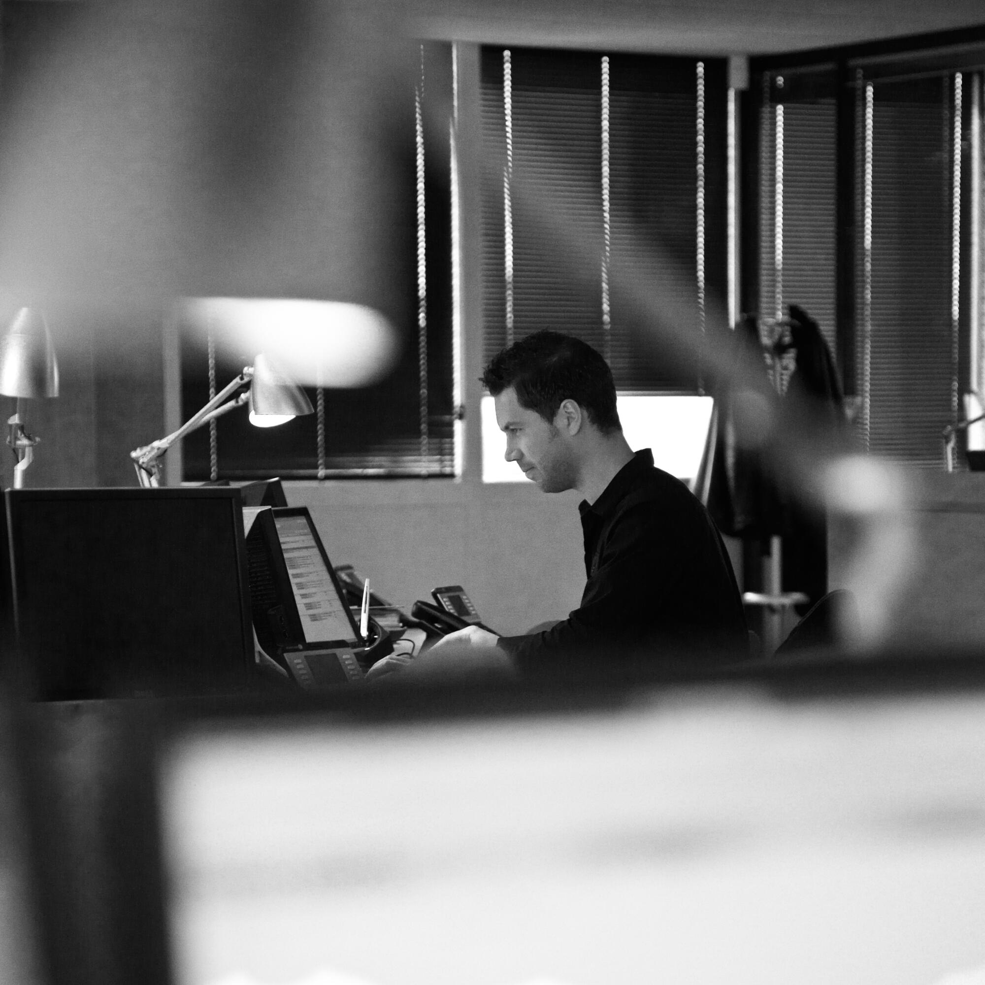 Photographie en noir et blanc d'un homme concentré travaillant sur un ordinateur dans un bureau. Par Studio ZE, photographe humain à Toulouse.