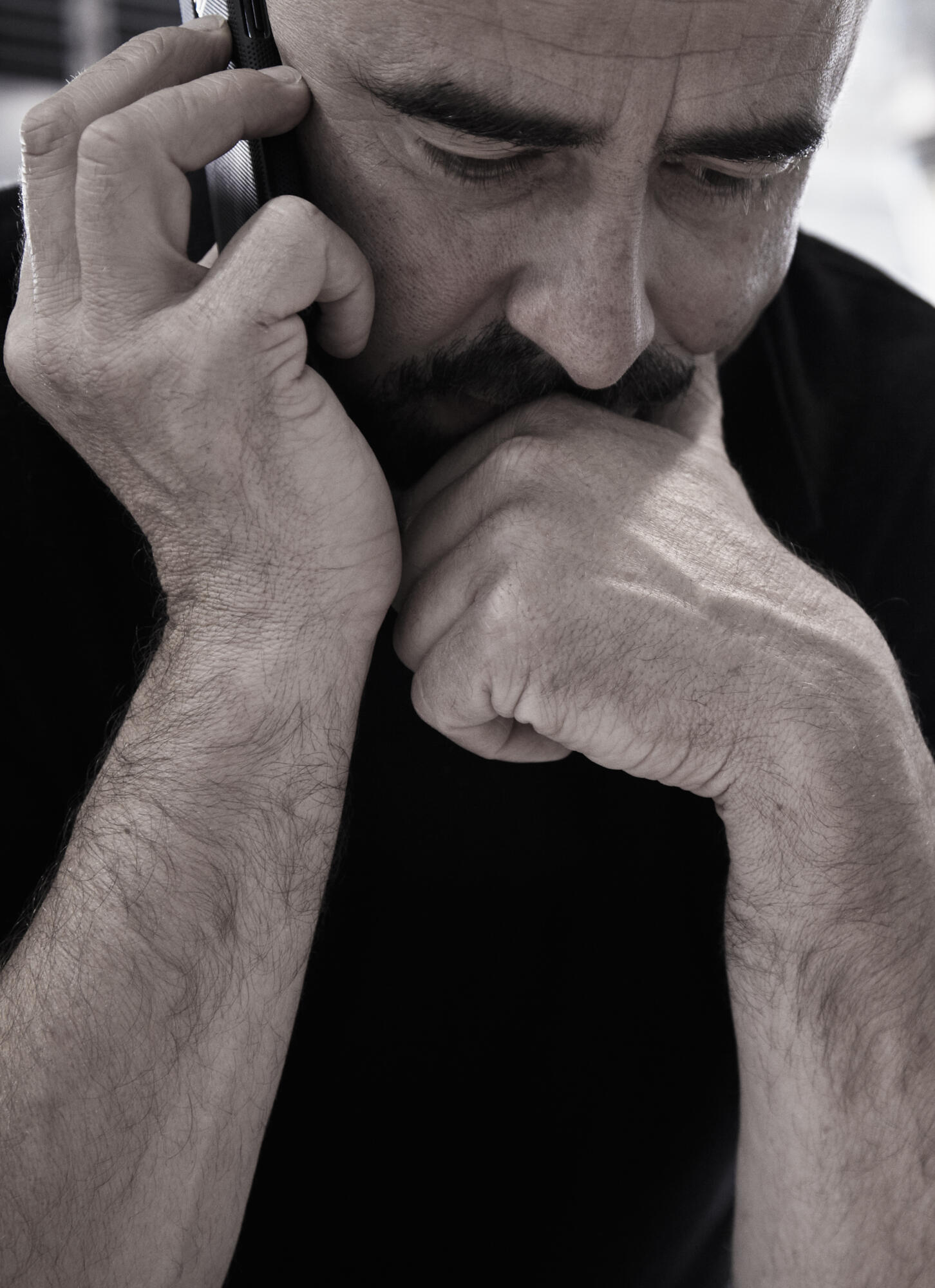 Photographie en noir et blanc d'un homme au téléphone, portrait serré, expression pensive. Par Studio ZE, photographe humain à Toulouse.
