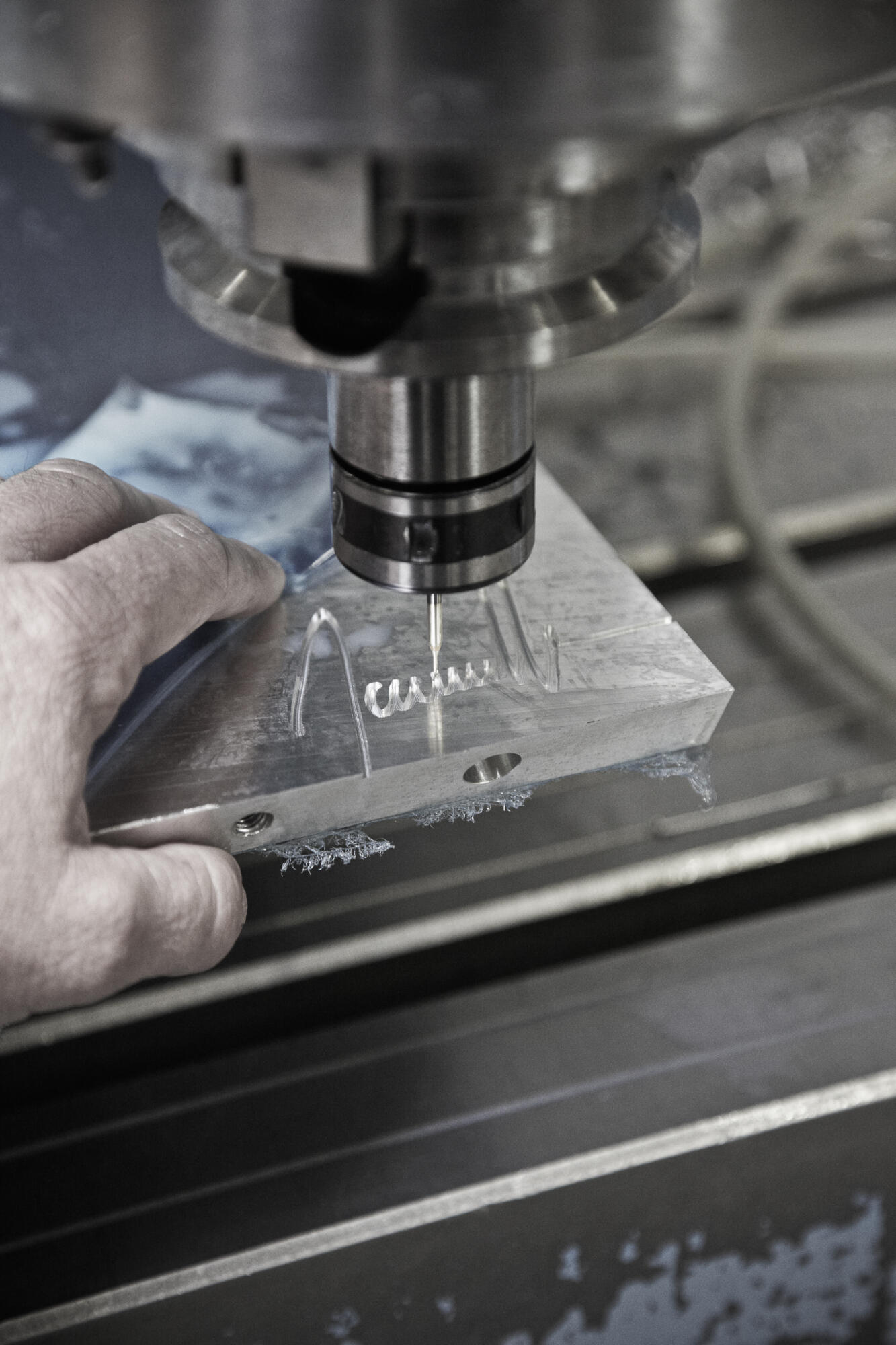 Photographie en gros plan d'une main d'ouvrier ajustant une pièce sur une machine CNC en fonctionnement. Par Studio ZE, photographe humain à Toulouse.