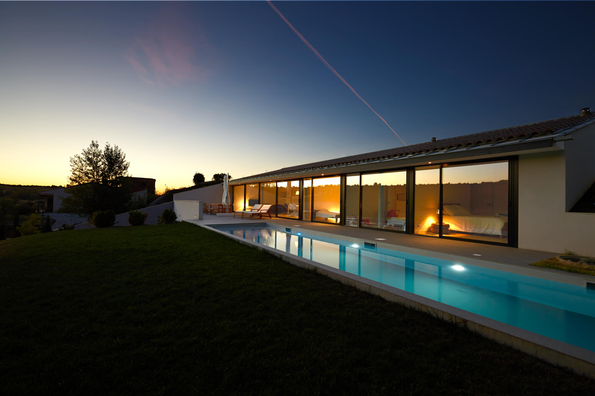 Photographie d'une villa moderne avec longue piscine illuminée au crépuscule. Par Studio ZE, photographe d'architecture et de biens immobiliers à Toulouse.