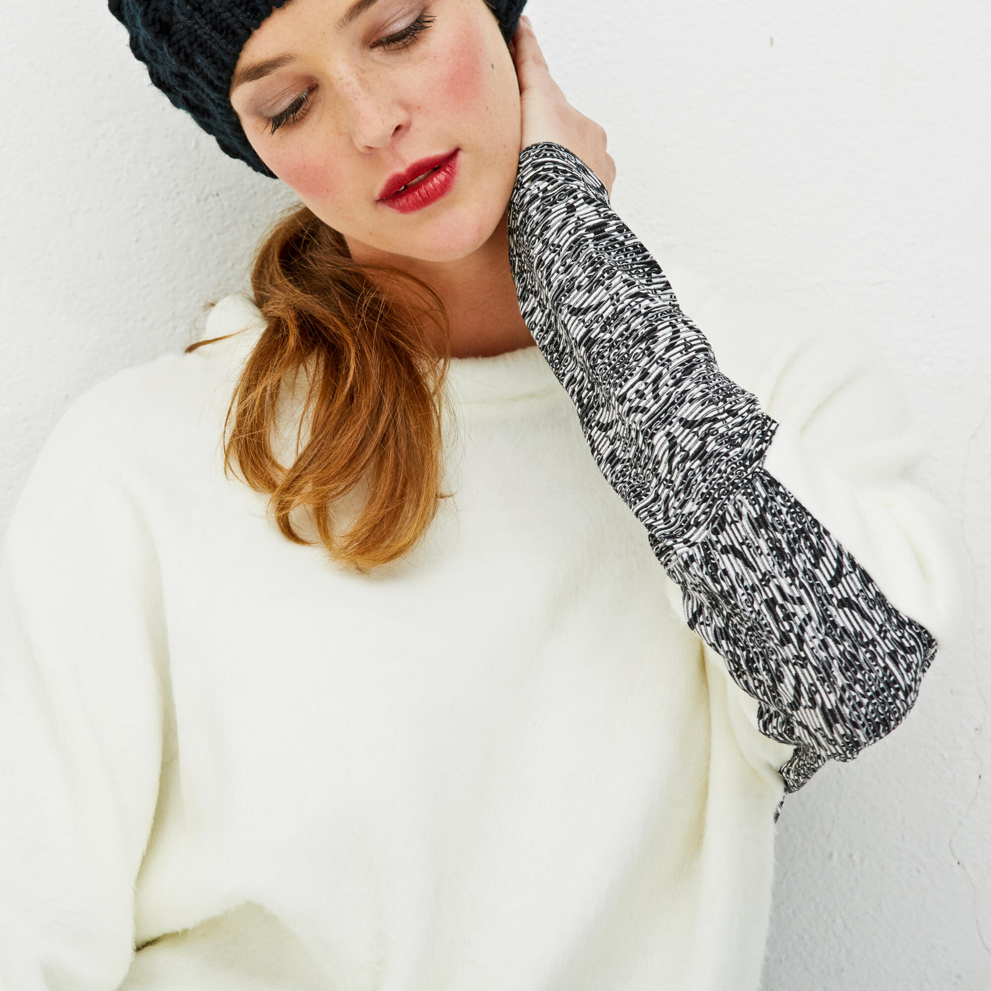 Photographie d'une femme aux cheveux roux, vêtue d'un pull blanc douillet et d'un bonnet noir, avec un motif graphique sur la manche. Par Studio ZE, photographe mode à Toulouse.