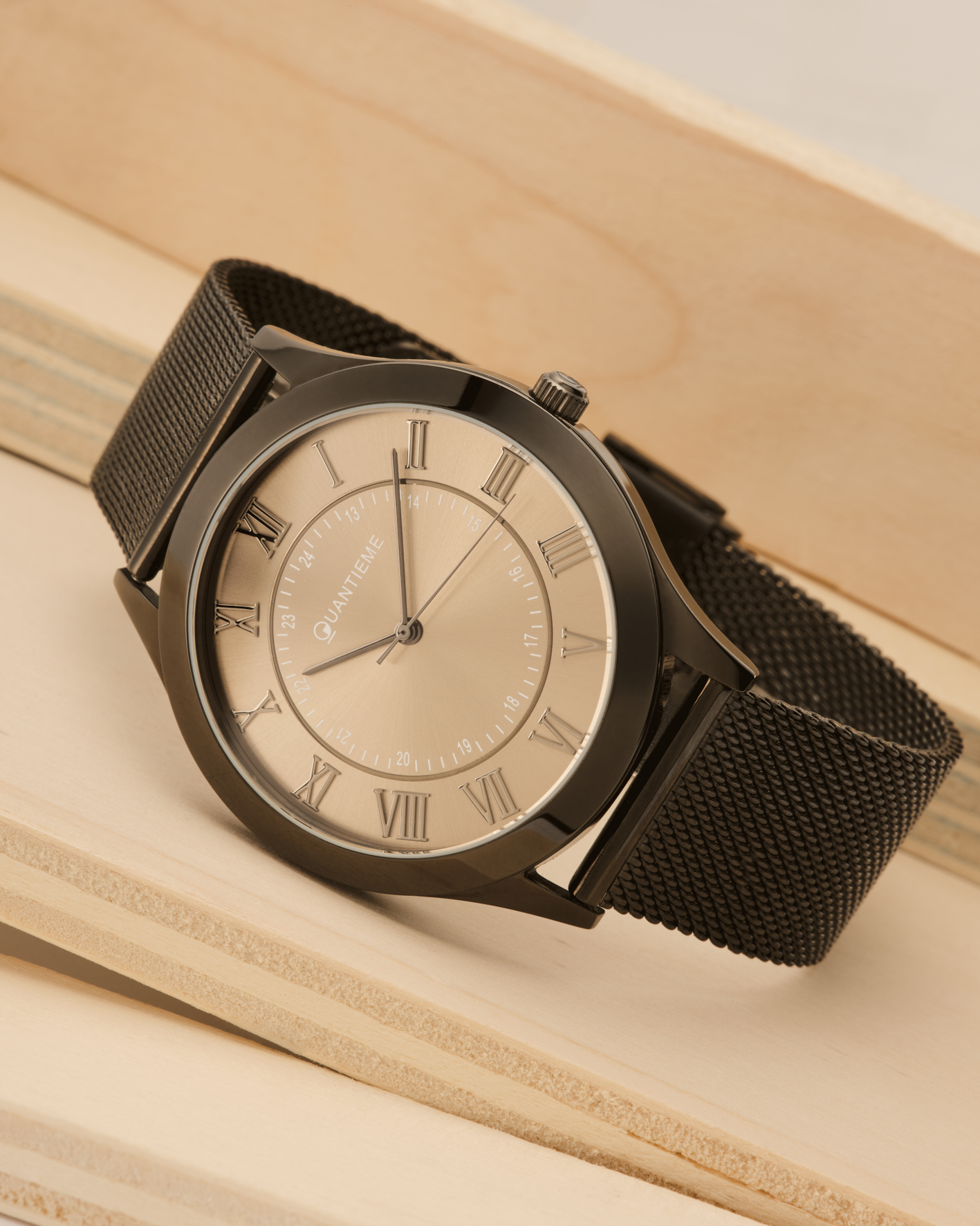 Photographie détaillée d'une montre homme cadran doré, bracelet maille noir, sur fond bois clair. Par Studio ZE, photographe bijoux à Toulouse.