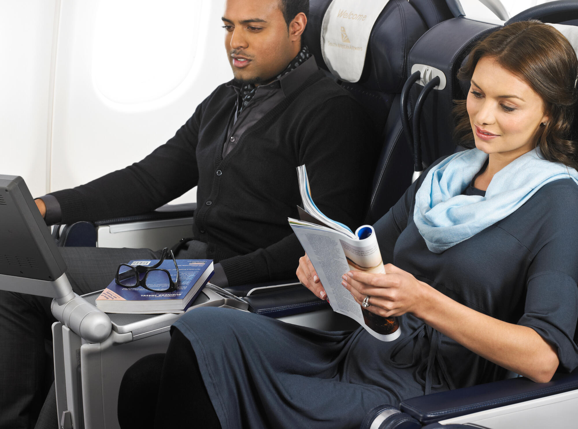 Photographie de deux passagers adultes dans un avion, une femme lisant un magazine et un homme regardant un écran. Par Studio ZE, photographe humain à Toulouse.