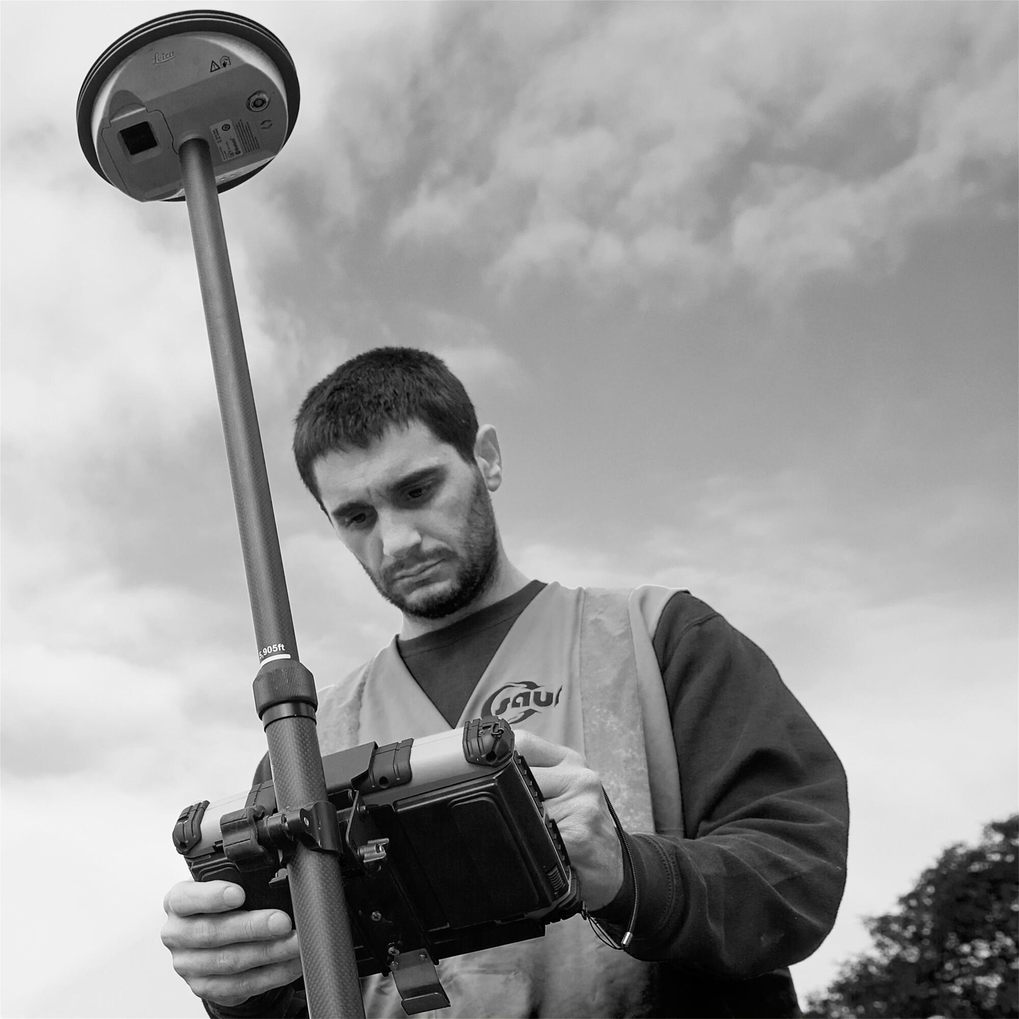 Photographie en noir et blanc d'un homme en tenue de travail manipulant un équipement de mesure topographique. Par Studio ZE, photographe humain à Toulouse.