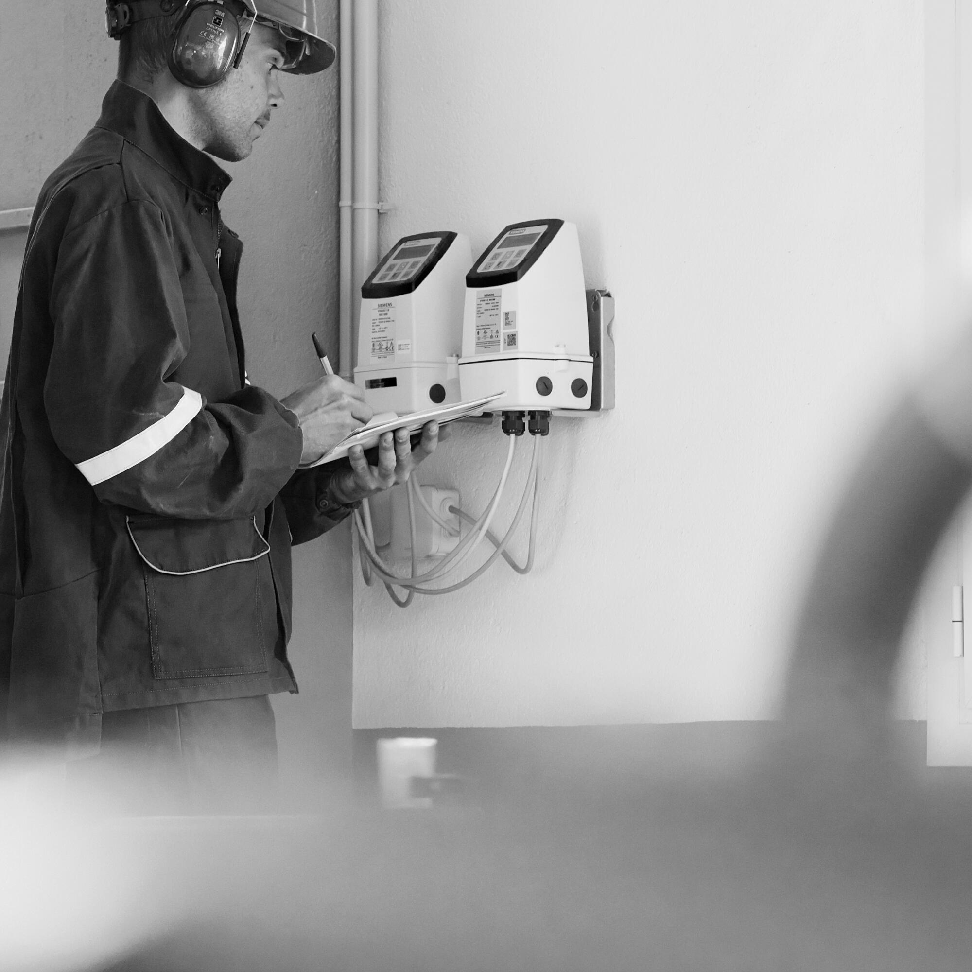 Photographie en noir et blanc d'un homme en tenue de travail avec casque anti-bruit, prenant des notes devant un équipement industriel. Par Studio ZE, photographe humain à Toulouse.