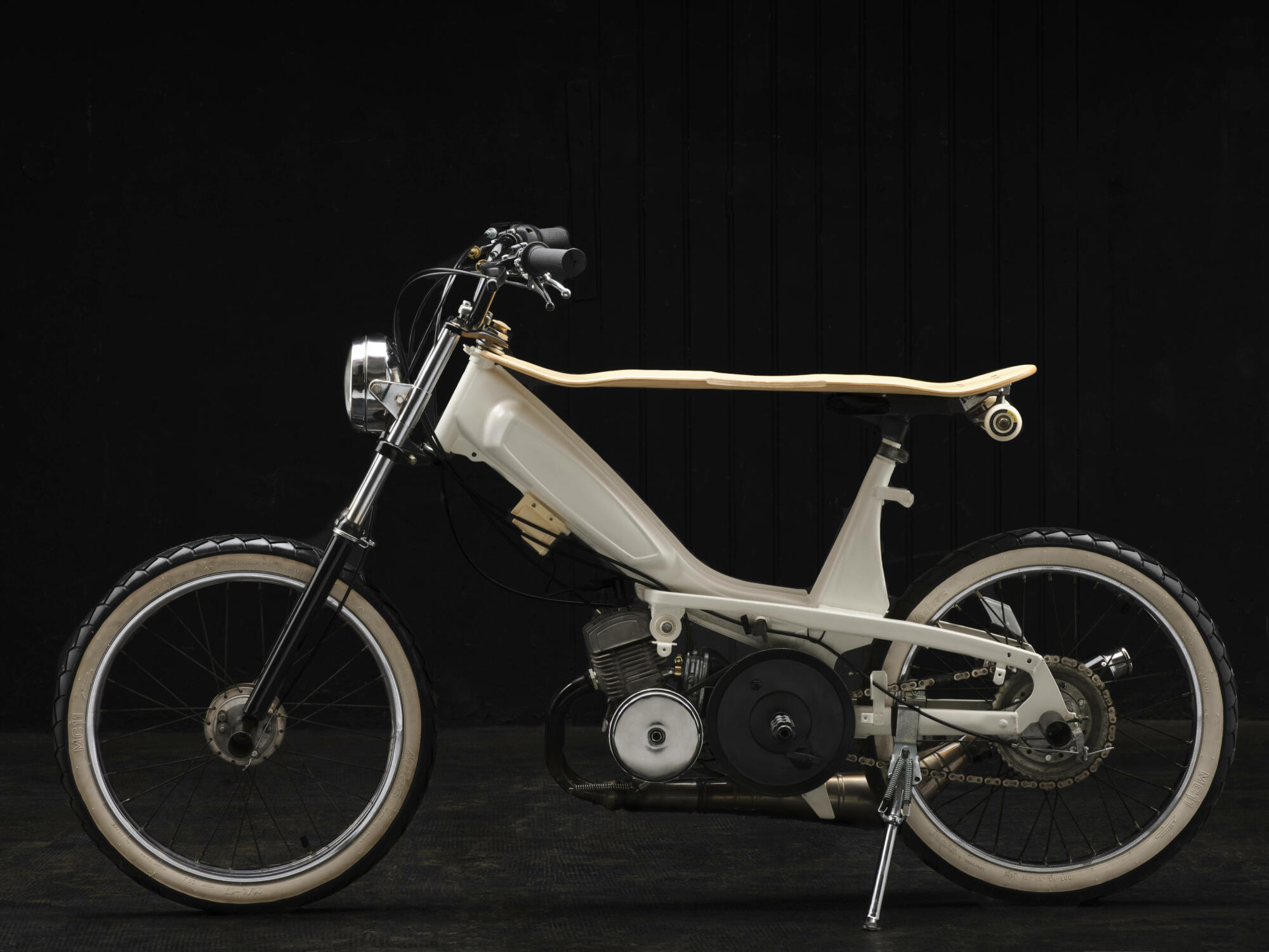 Photographie d'une mobylette customisée blanche avec une planche de skate en bois en guise de selle, sur fond noir. Par Studio ZE, photographe auto moto à Toulouse.