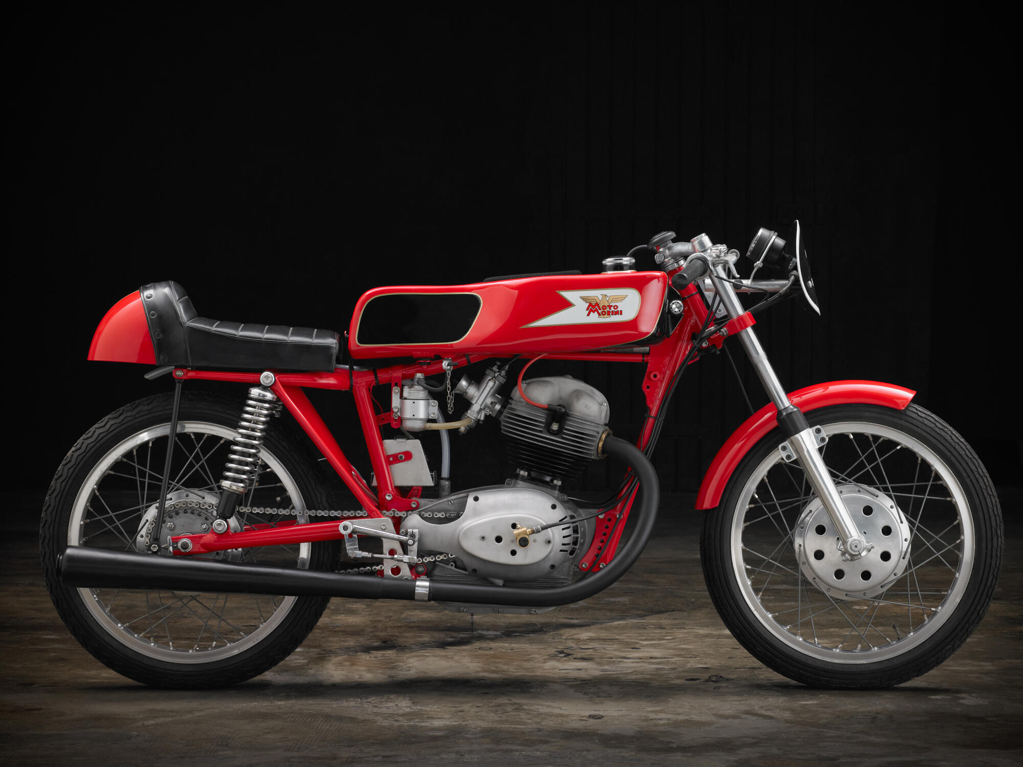 Photographie d'une moto de course rouge et noire au style vintage, avec des éléments chromés et le logo sur le réservoir, sur fond noir. Par Studio ZE, photographe auto moto à Toulouse.