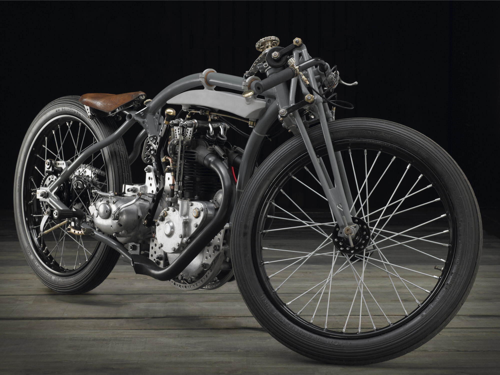 Photographie d'une moto customisée grise et marron au design vintage, avec un siège en cuir et des roues à rayons, sur fond sombre. Par Studio ZE, photographe auto moto à Toulouse.