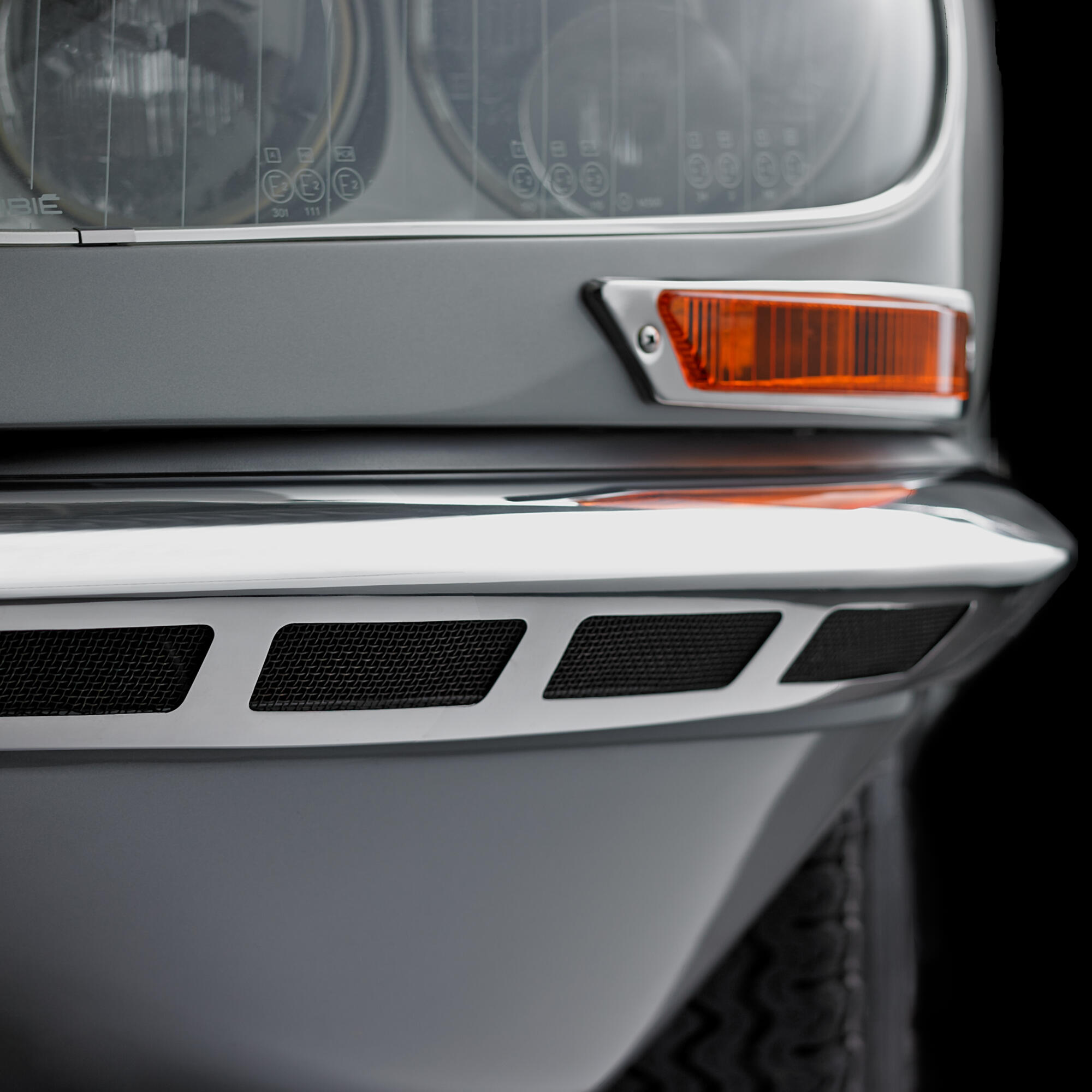 Photographie en gros plan d'un phare avant de voiture ancienne, avec des grilles et un clignotant orange. Par Studio ZE, photographe auto moto à Toulouse.