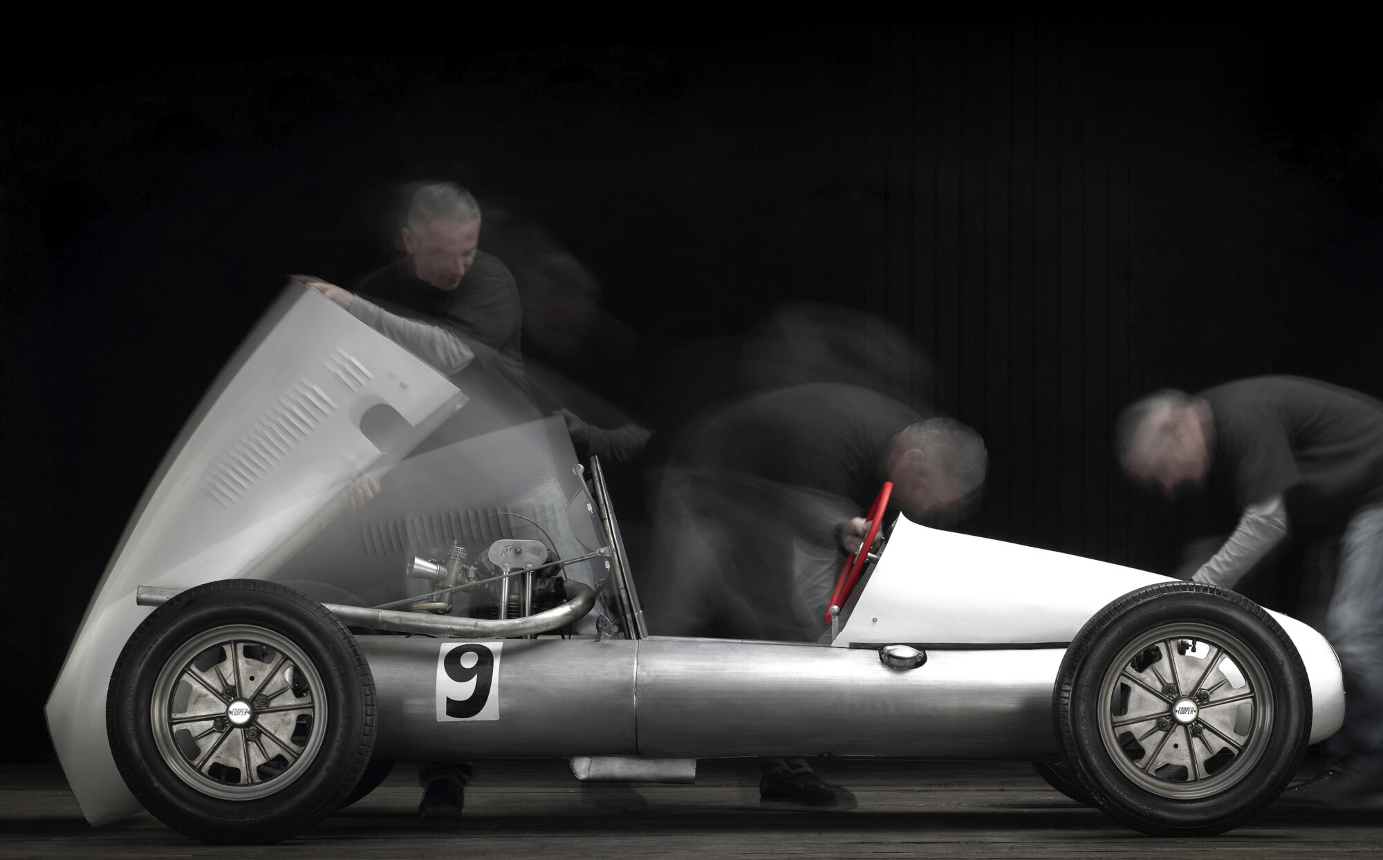 Photographie d'une voiture de course monoplace ancienne de couleur claire avec le chiffre '9', avec des effets de mouvement suggérant une activité autour. Par Studio ZE, photographe auto moto à Toulouse.
