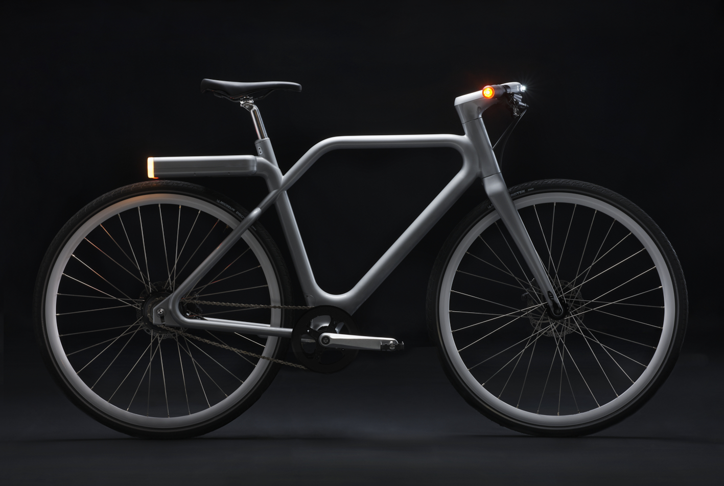 Photographie d'un vélo gris au design épuré, avec éclairage avant et arrière intégré, sur fond sombre. Par Studio ZE, photographe auto moto à Toulouse.