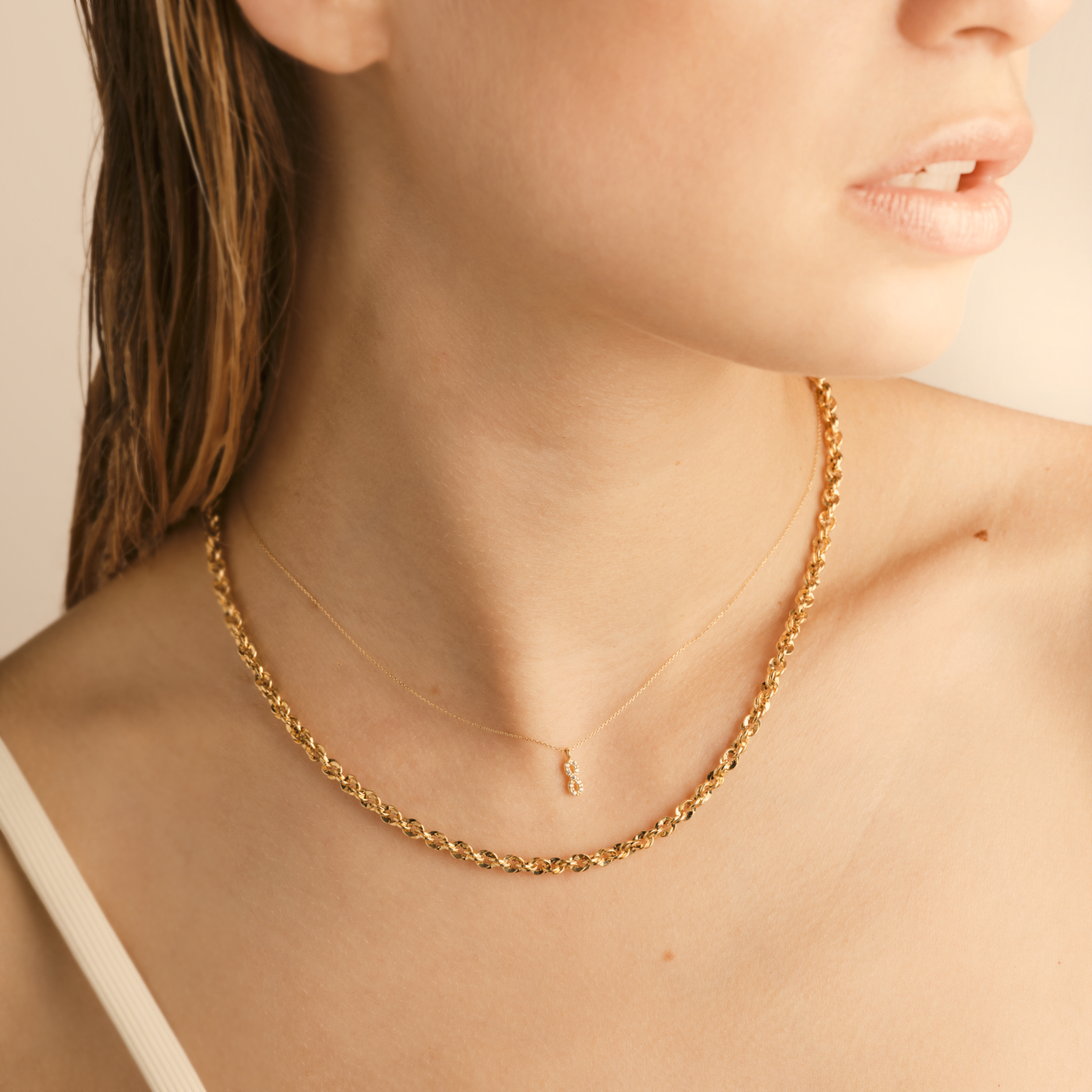 Photographie d'une femme portant deux colliers dorés : une chaîne épaisse à maillons et un pendentif fin. Par Studio ZE, photographe bijoux à Toulouse.