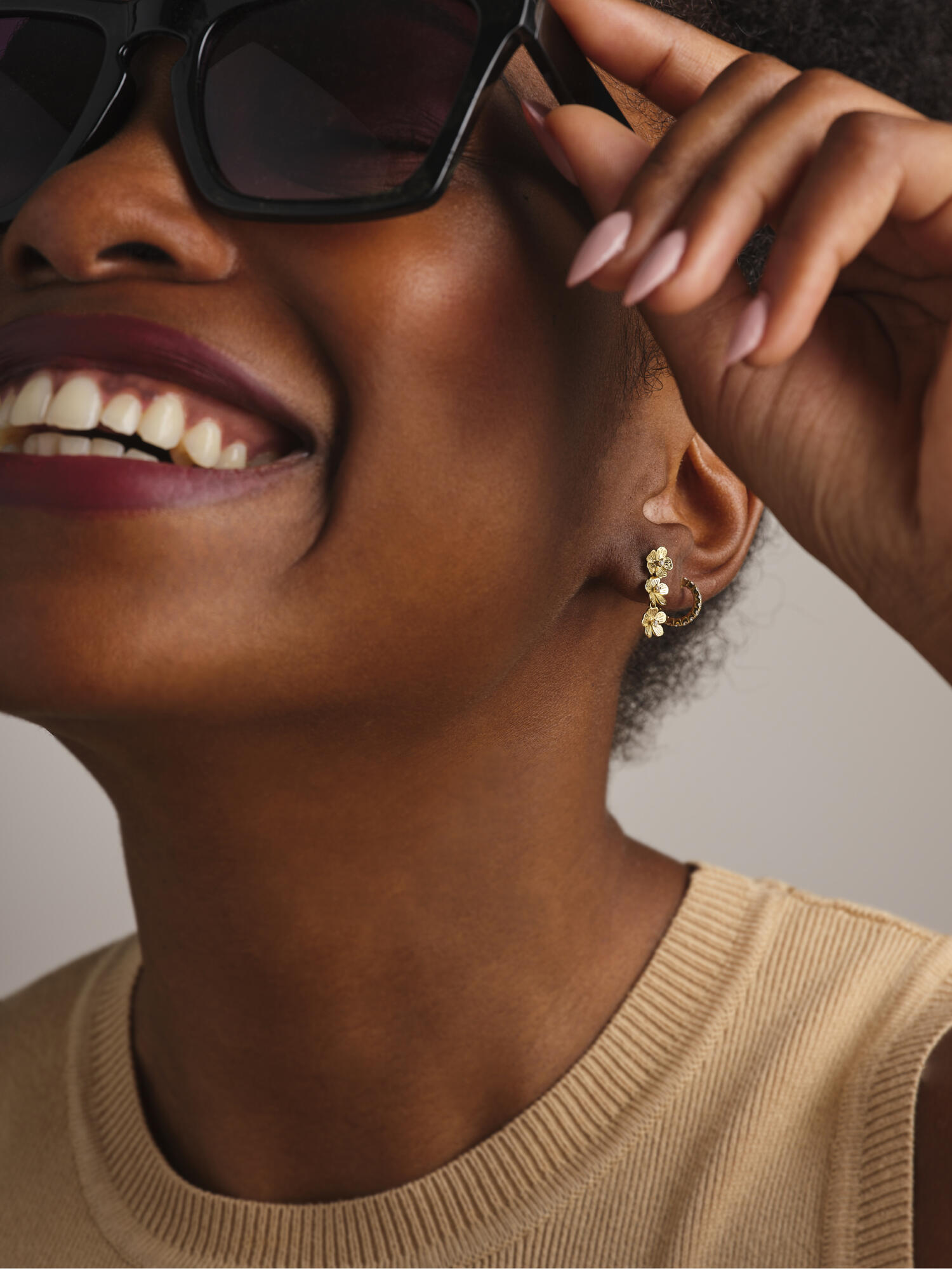 Photographie en gros plan d'une femme souriante, portant des lunettes de soleil noires et une boucle d'oreille dorée à motifs floraux. Par Studio ZE, photographe humain à Toulouse.