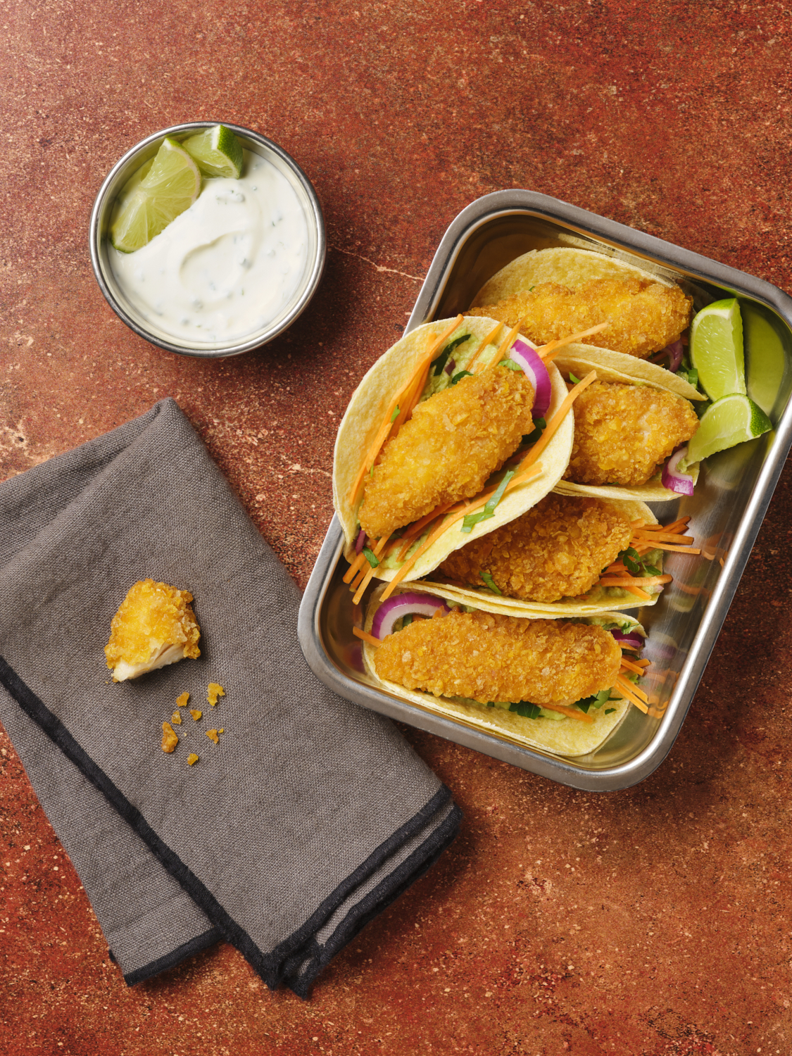 Photographie de tacos au poulet frit garnis de légumes, avec sauce crémeuse et quartiers de citron vert. Par Studio ZE, photographe culinaire à Toulouse.