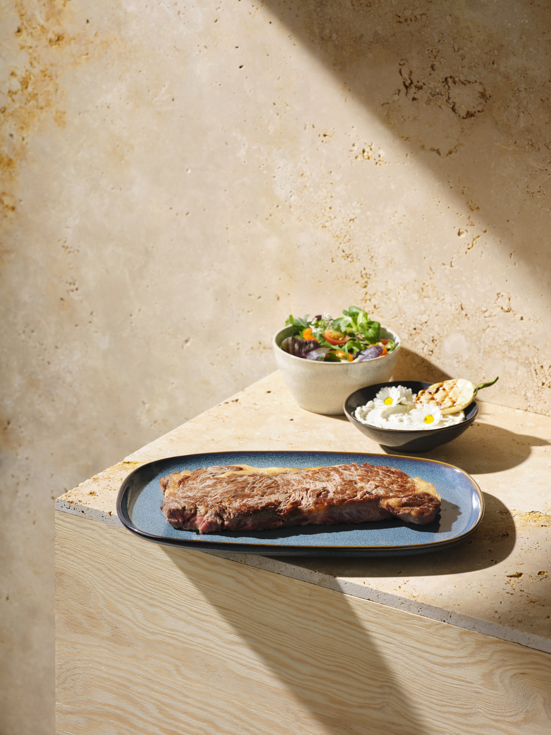 Photographie d'un faux filet grillé sur une assiette bleue, avec une salade fraîche et une sauce aux fleurs. Par Studio ZE, photographe culinaire à Toulouse.