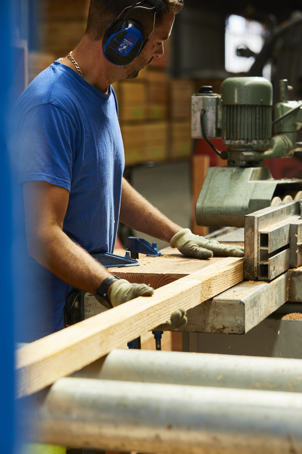 Photographie d'un homme en tenue de travail avec casque anti-bruit, travaillant sur une machine de découpe de bois dans une scierie. Par Studio ZE, photographe humain à Toulouse.